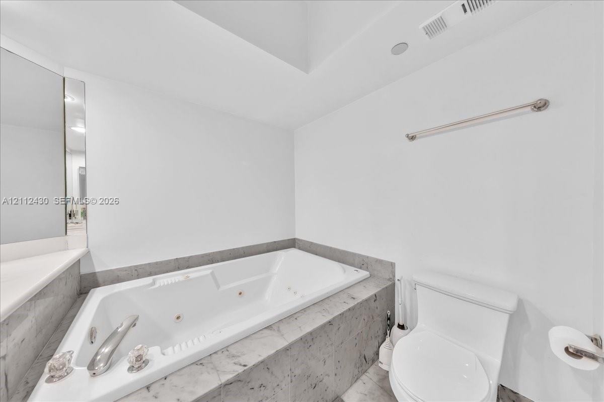 Built-in jetted tub with a tiled surround, chrome faucet hardware, and wall-mounted towel bar
