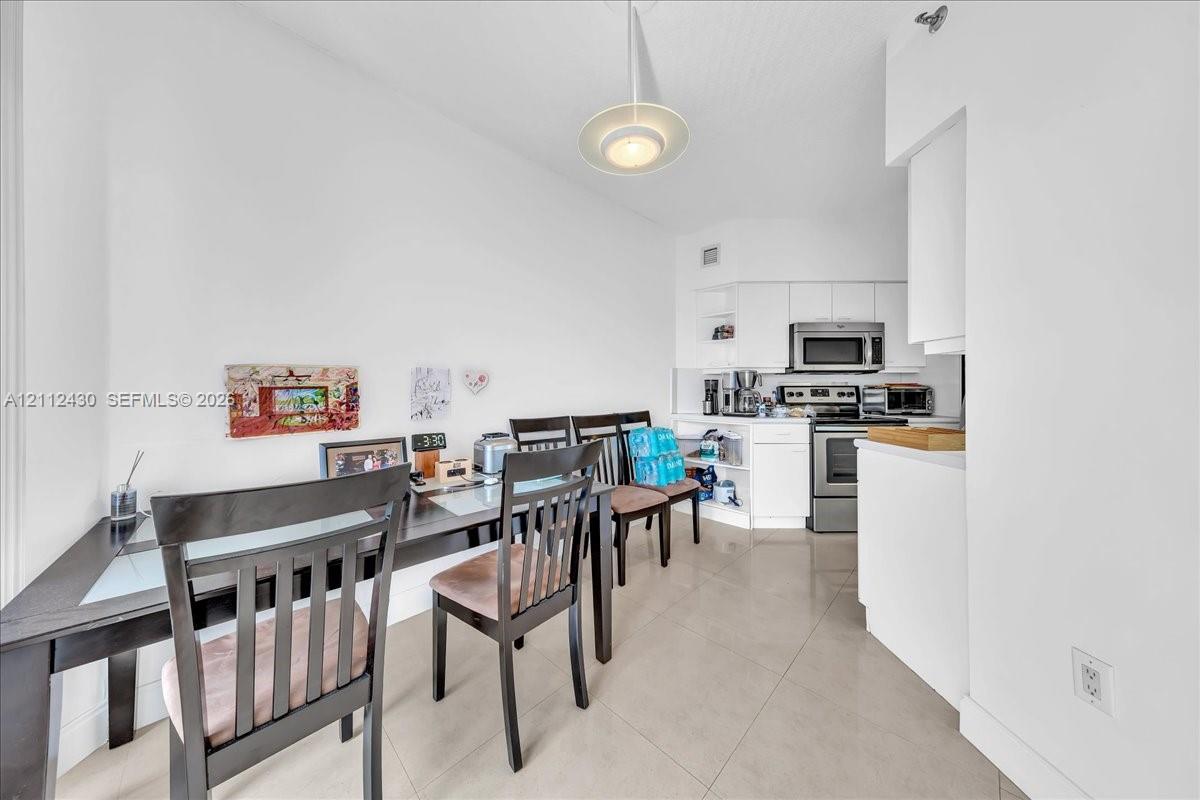 Kitchen area featuring white cabinetry, stainless steel appliances, large-format tile flooring, and a contemporary pendant light fixture Kitchen area featuring white cabinetry, stainless steel appliances, large-format tile flooring, and a contemporary pendant light fixture