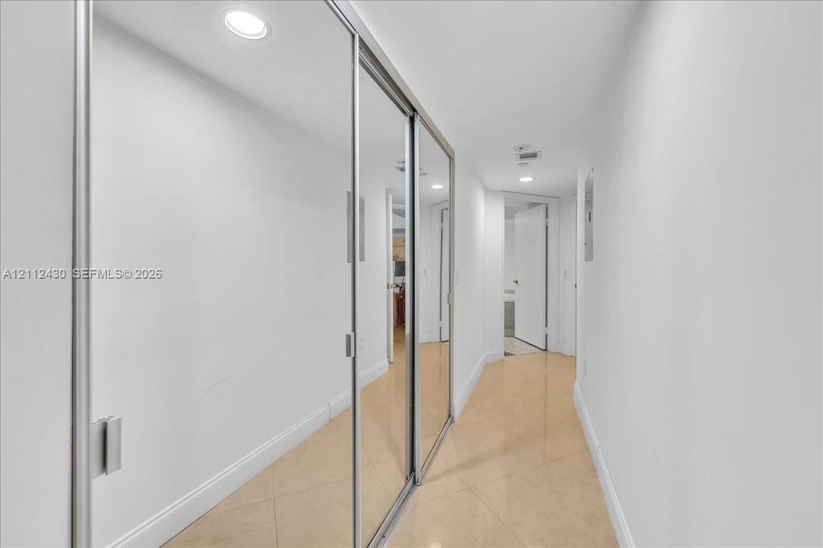 Hallway featuring floor-to-ceiling mirrored sliding closet doors, neutral tile flooring, and recessed lighting