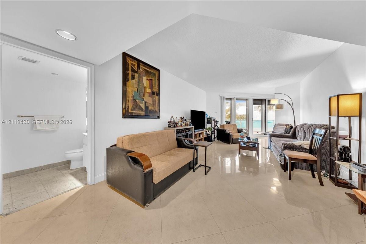 Open-concept interior featuring large-format tile flooring, recessed lighting, and a glass-paneled entry to an exterior space Open-concept interior featuring large-format tile flooring, recessed lighting, and a glass-paneled entry to an exterior space