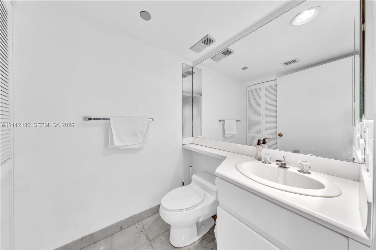 Vanity with an integrated sink and countertop, full-width wall mirror, and stone-finish flooring
