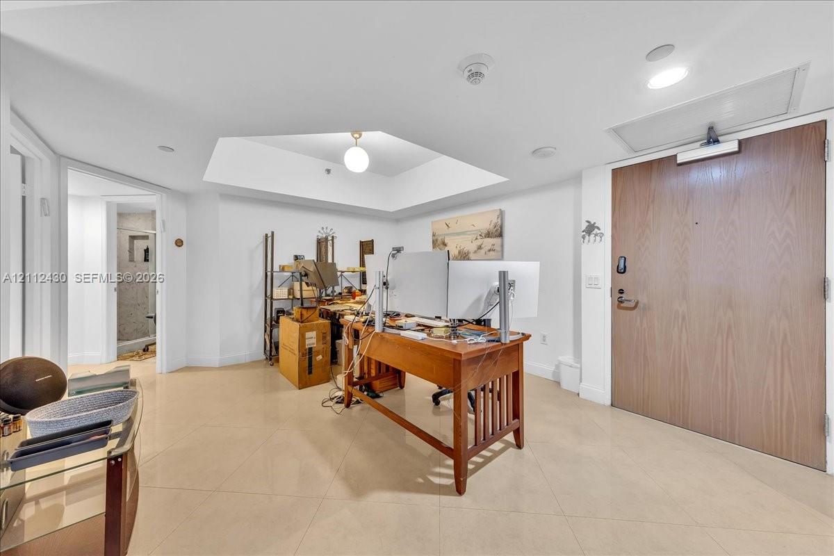 Large room featuring a coffered ceiling, recessed lighting, neutral tile flooring, and a solid wood entry door with a heavy-duty hydraulic door closer Large room featuring a coffered ceiling, recessed lighting, neutral tile flooring, and a solid wood entry door with a heavy-duty hydraulic door closer
