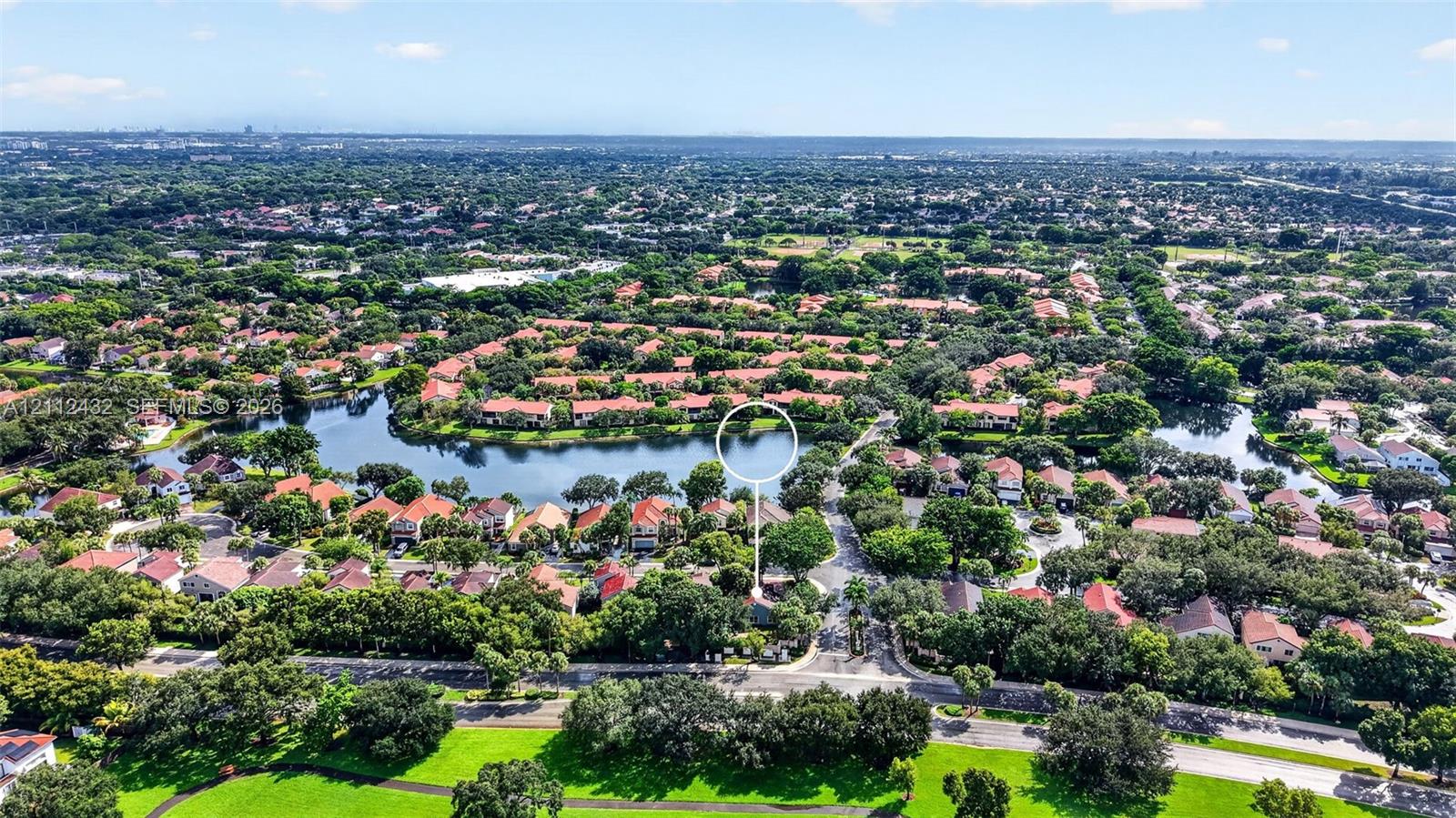 Aerial perspective of a waterfront property featuring a central lake, extensive tree canopy, and dense residential landscaping