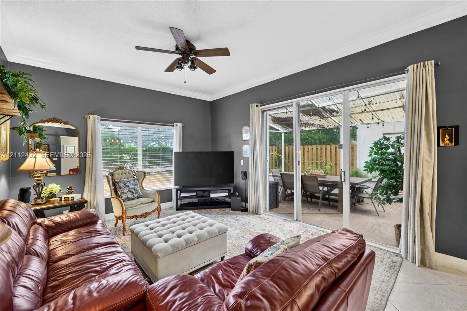 Living area featuring tile flooring, crown molding, a ceiling fan, and large sliding glass doors opening to a covered patio