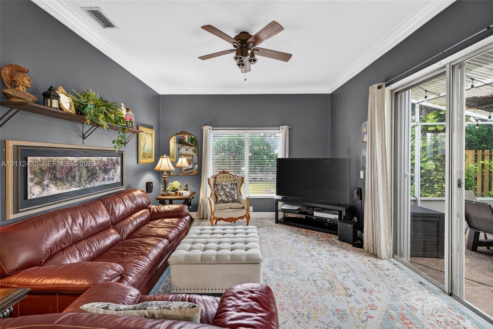 Living space featuring crown molding, neutral wall color, a multi-blade ceiling fan, and sliding glass doors