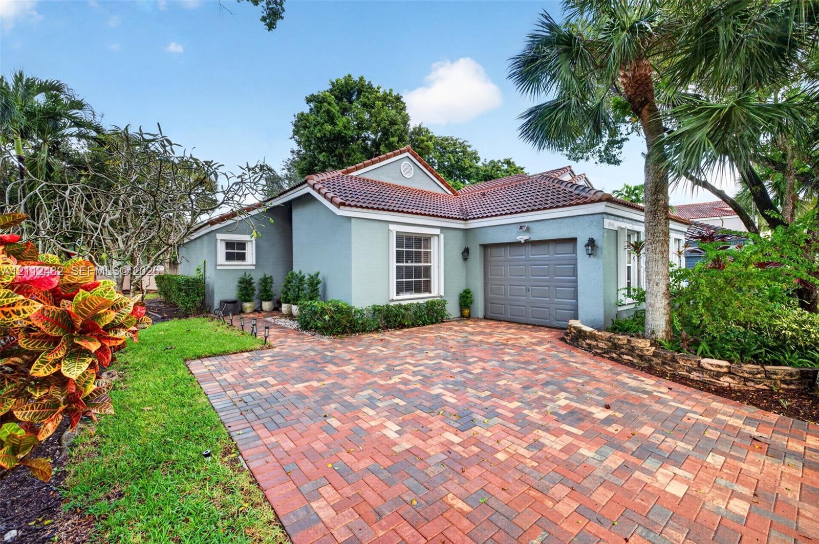 Single-story exterior featuring a multi-toned brick paver driveway, tile roof, and stone-accented landscaping