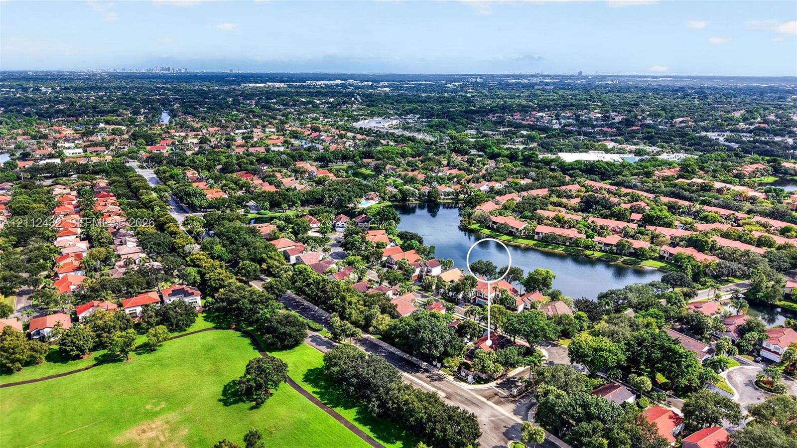 Aerial perspective featuring a residential property situated on a lakefront lot with mature canopy trees and expansive surrounding green space