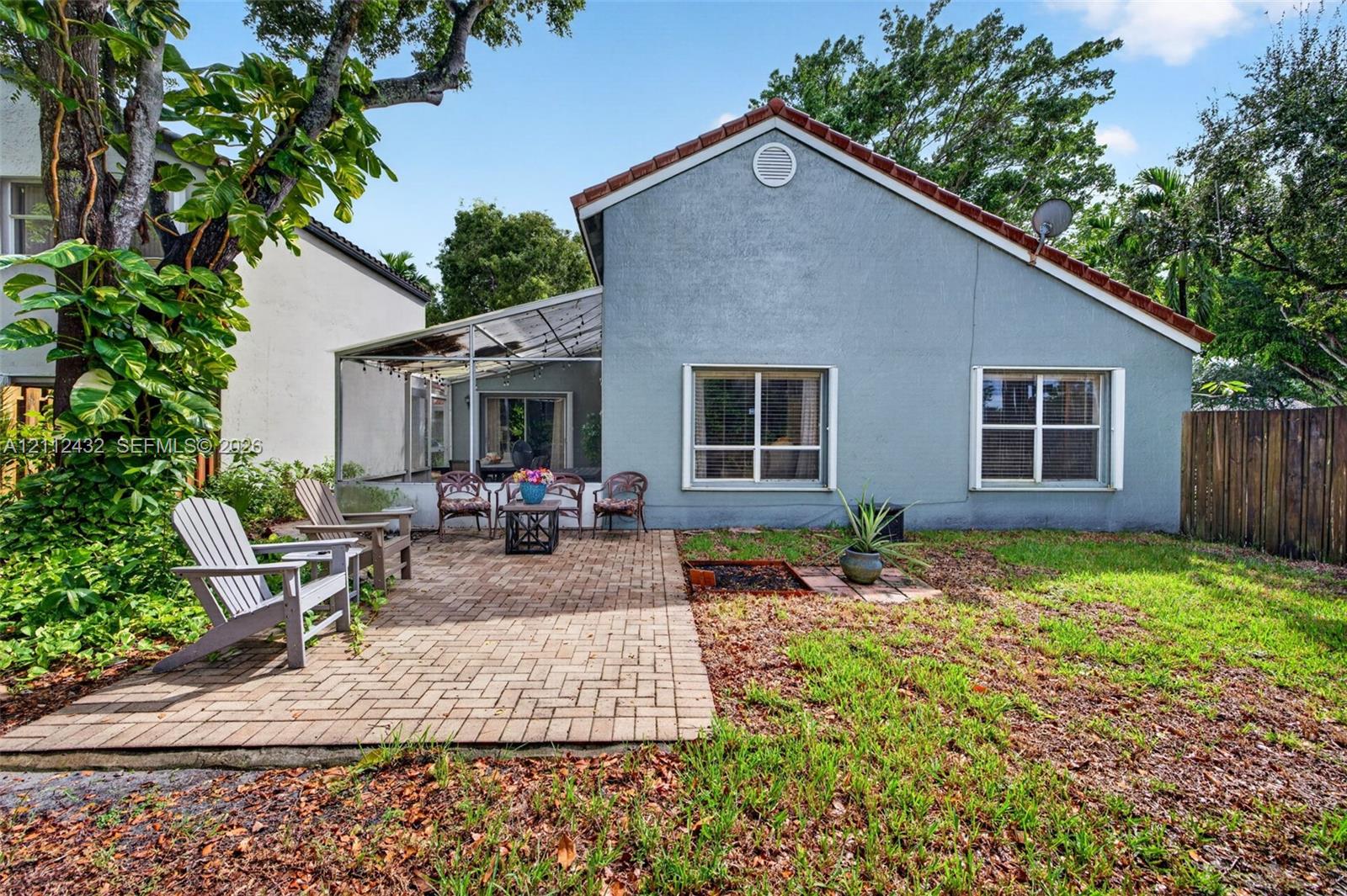 Rear exterior featuring a brick paver patio, screened-in enclosure, stucco siding, and a gabled roof