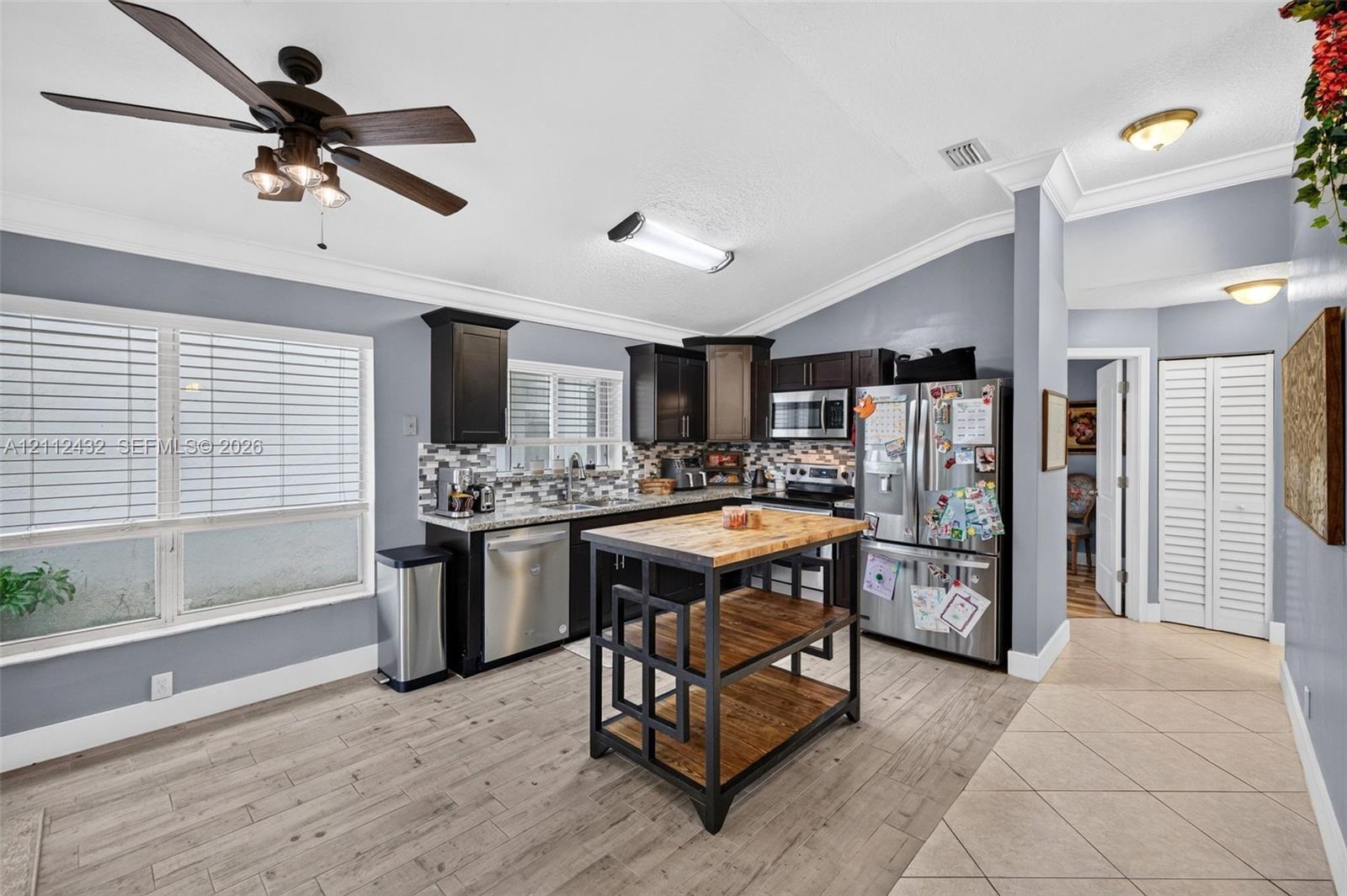 Kitchen featuring dark-toned cabinetry, stainless appliances, patterned backsplash, wood-look tile flooring, and crown molding