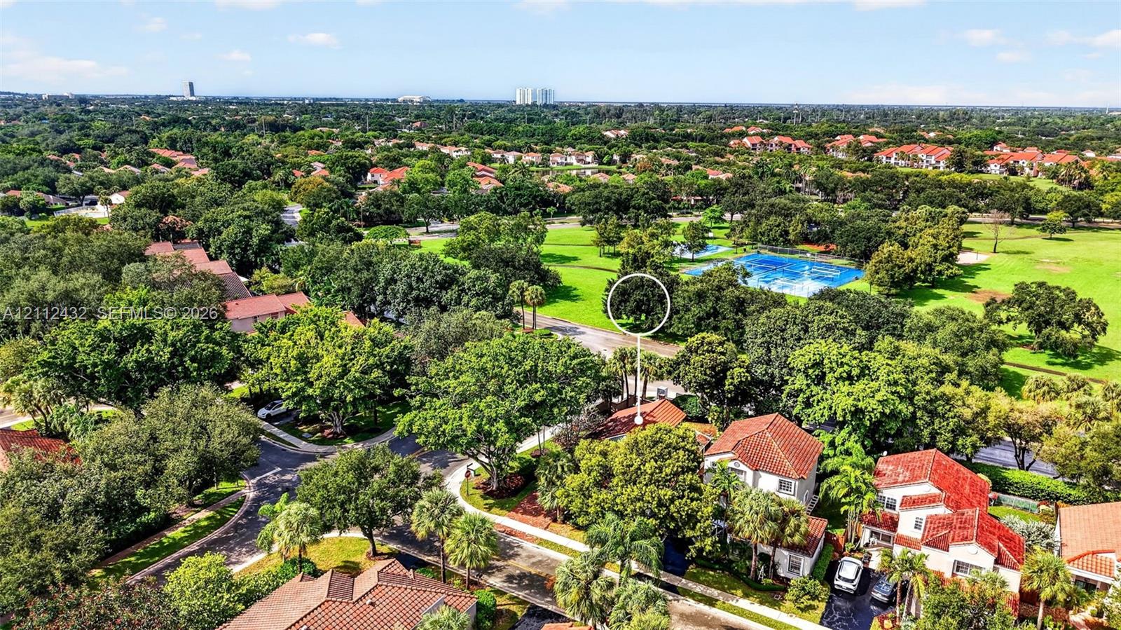 Aerial perspective showcasing a residential setting with mature tree canopy, tile roof architecture, and proximity to expansive green space
