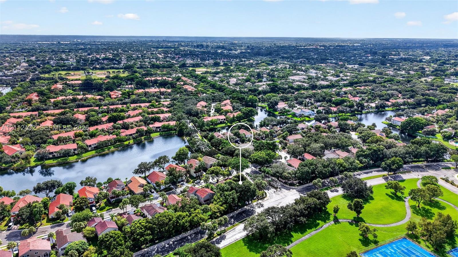 Aerial perspective featuring a residential lot with mature trees, situated within a community of tiled-roof structures featuring interspersed lakes and green spaces