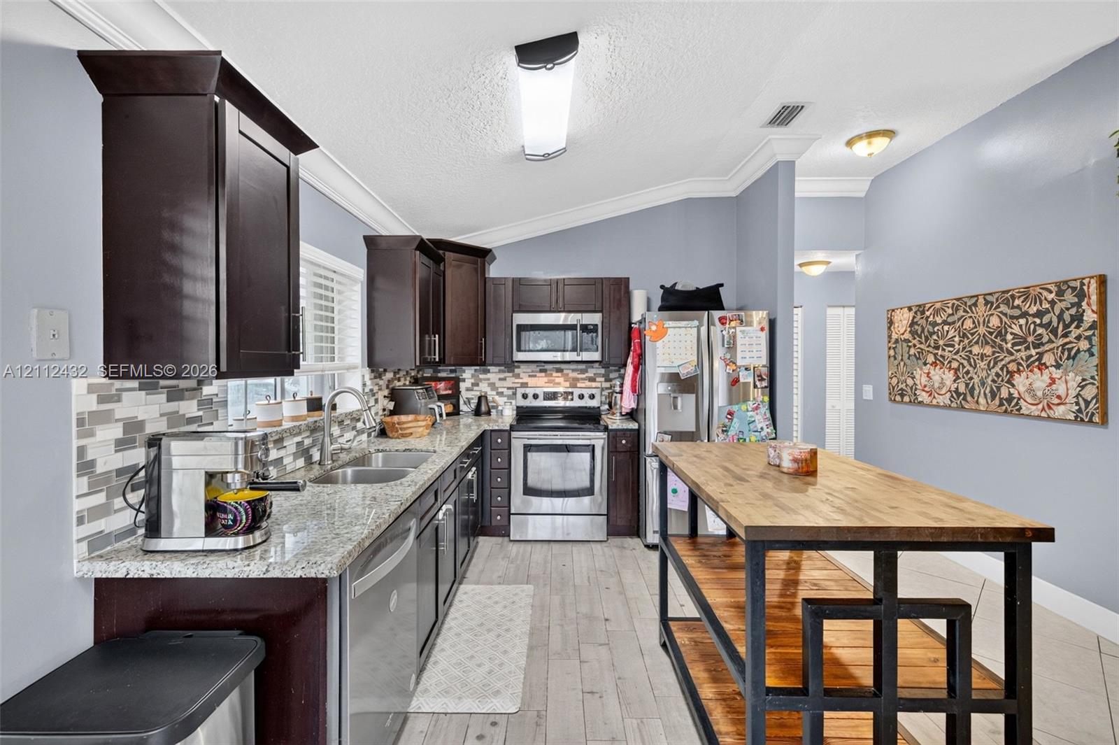Kitchen featuring dark cabinetry, stone countertops, a multi-tone tile backsplash, stainless appliances, and wood-look tile flooring