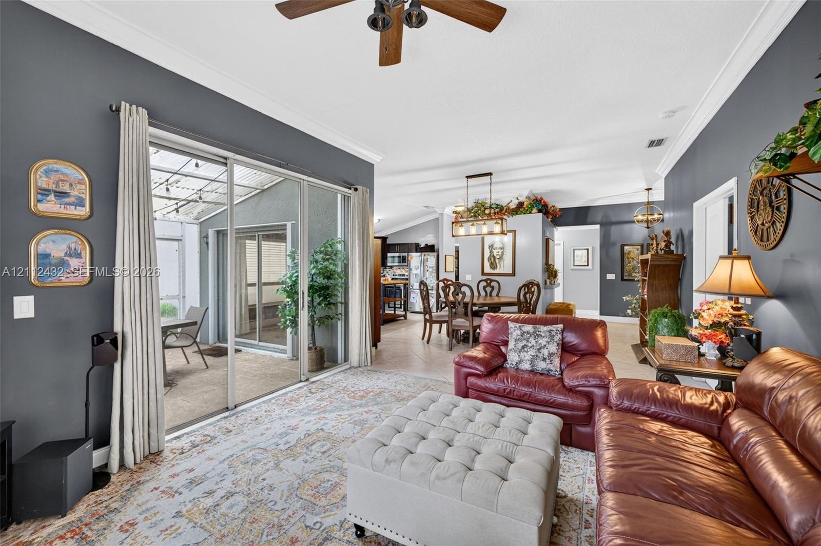 Living area featuring crown molding, neutral tile flooring, a multi-blade ceiling fan, and sliding glass doors opening to a covered patio