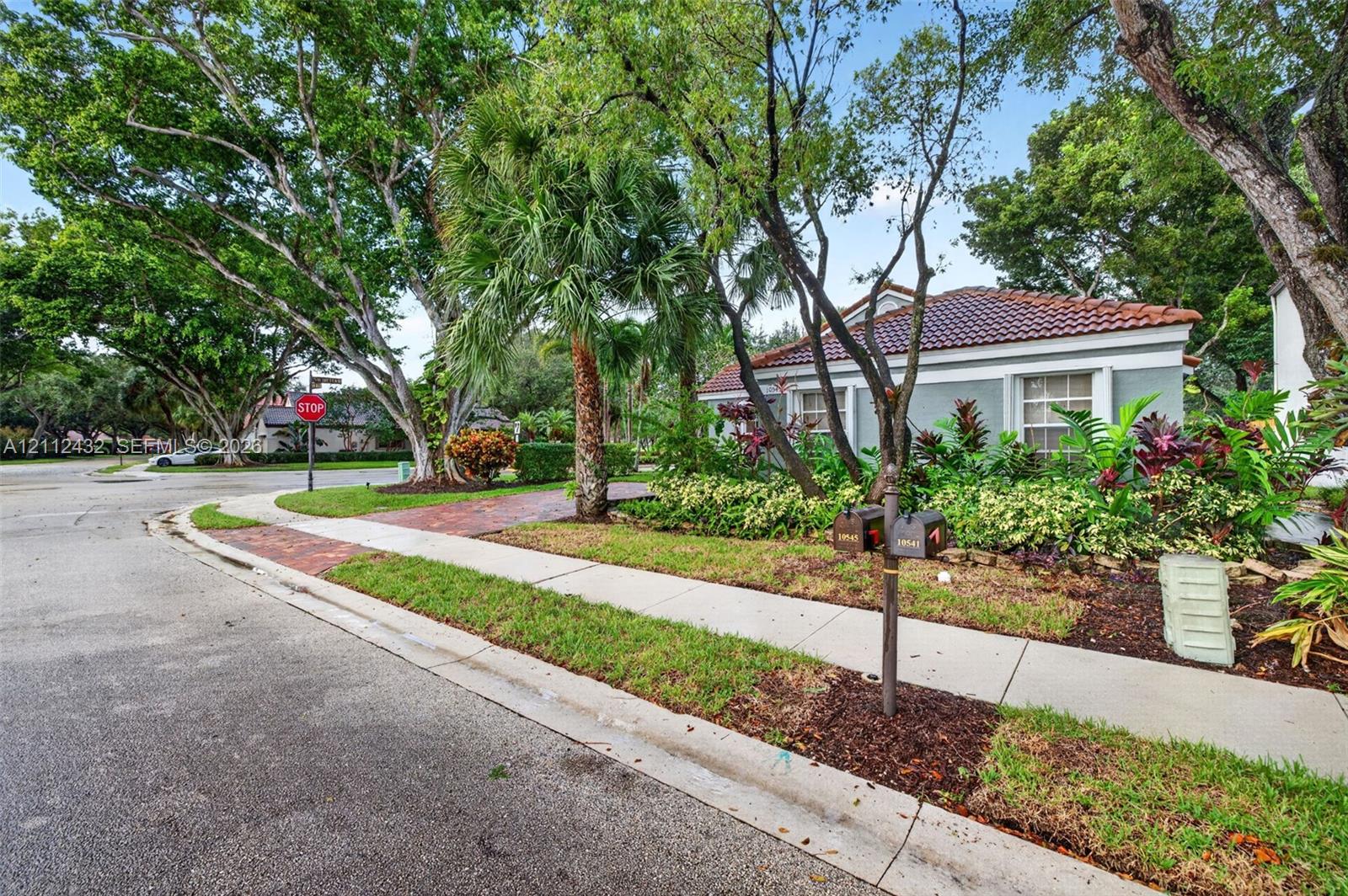 Exterior featuring a tile roof, brick-paved driveway, mature landscaping, and established trees