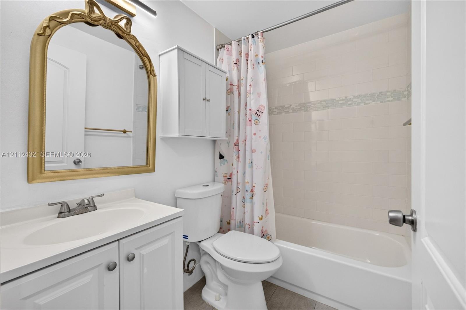 Bathroom featuring a white vanity cabinet with an integrated sink, a wall-mounted storage cabinet, a bathtub with tile surround, and an arched wall mirror