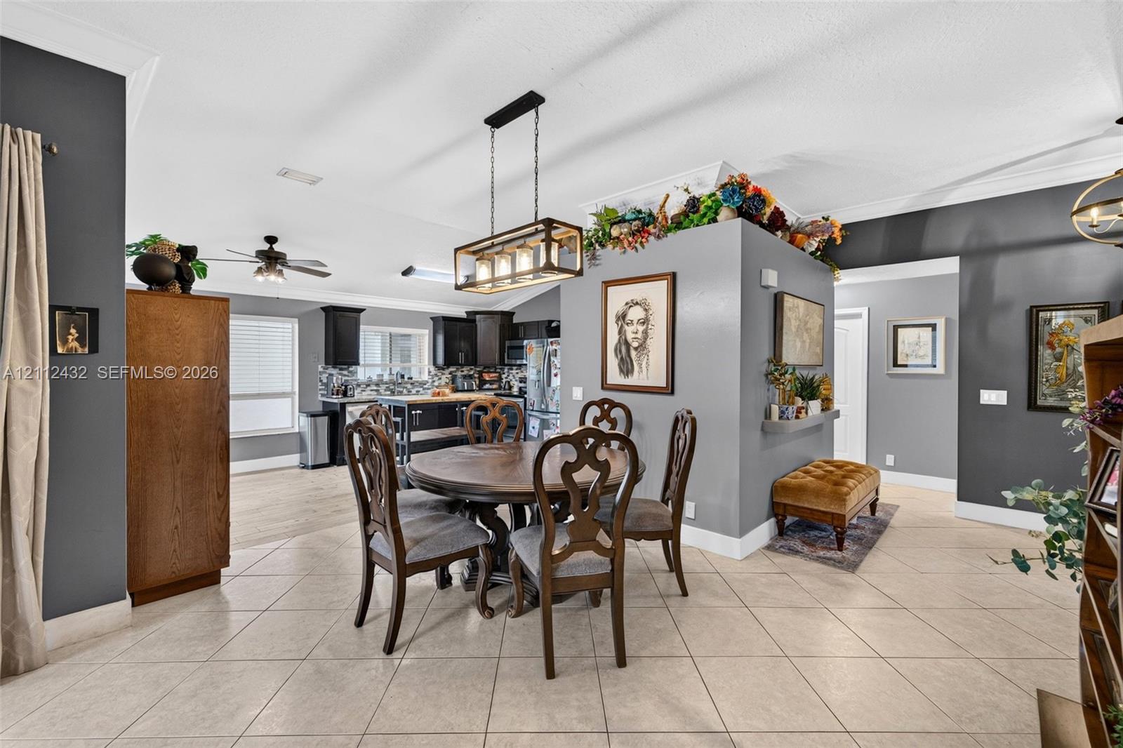 Open-concept interior featuring light-toned tile flooring, a central decorative wall divider, a rectangular multi-light pendant fixture, and crown molding