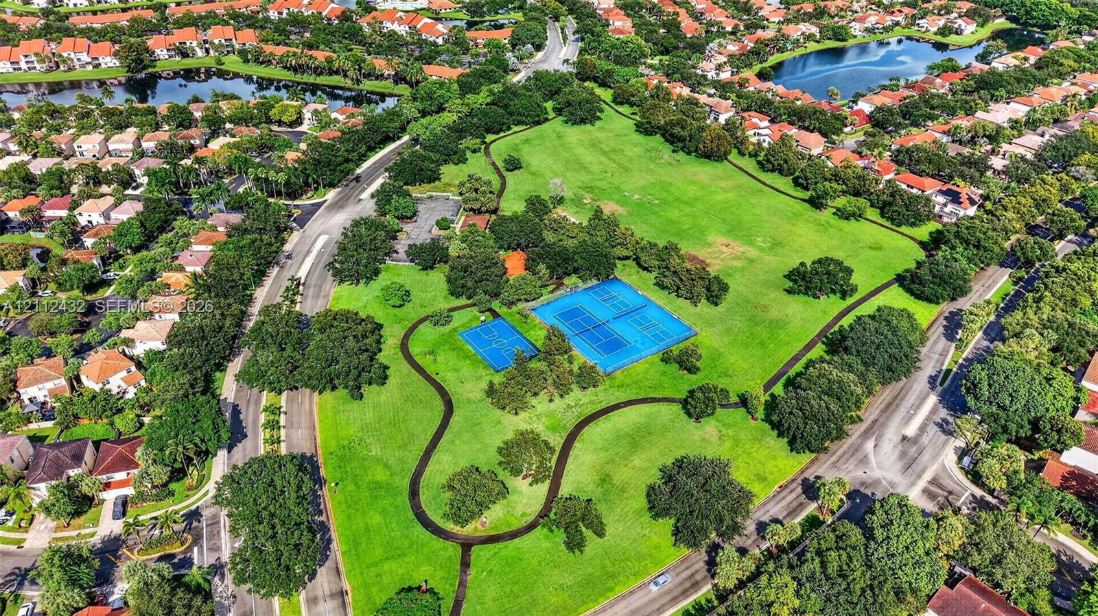 Expansive green space featuring tennis courts, a basketball court, mature trees, and paved walking paths