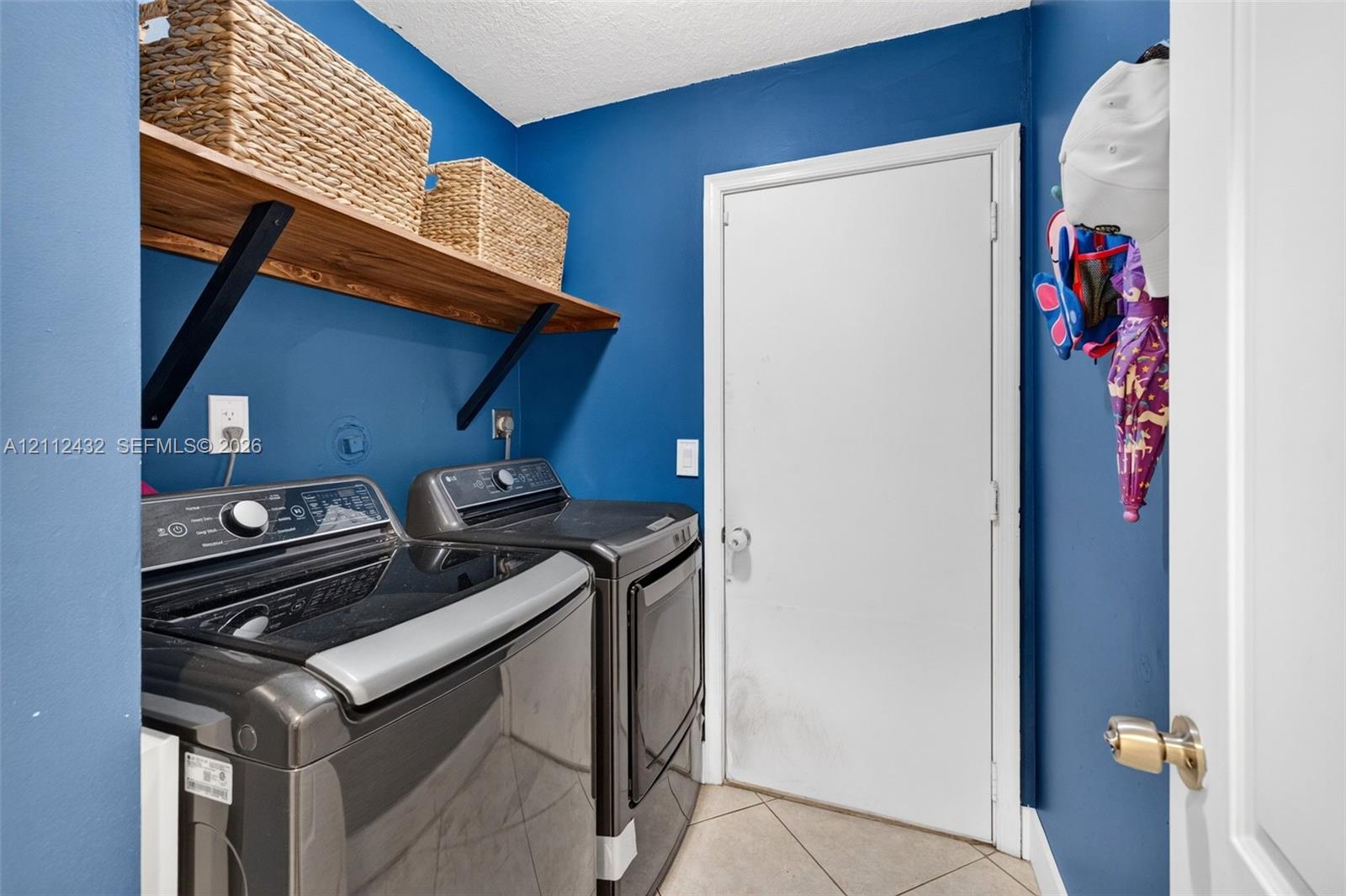 Laundry area featuring large-format diagonal tile flooring, mounted natural wood look shelving