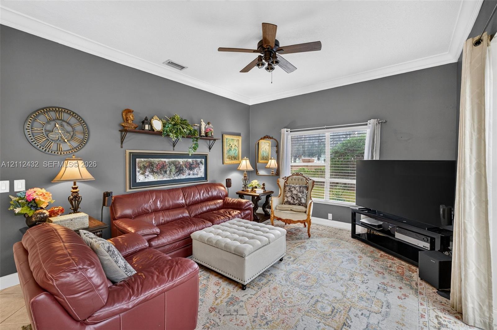 Living area featuring crown molding, neutral wall finishes, tile flooring, and a ceiling-mounted fan with integrated lighting