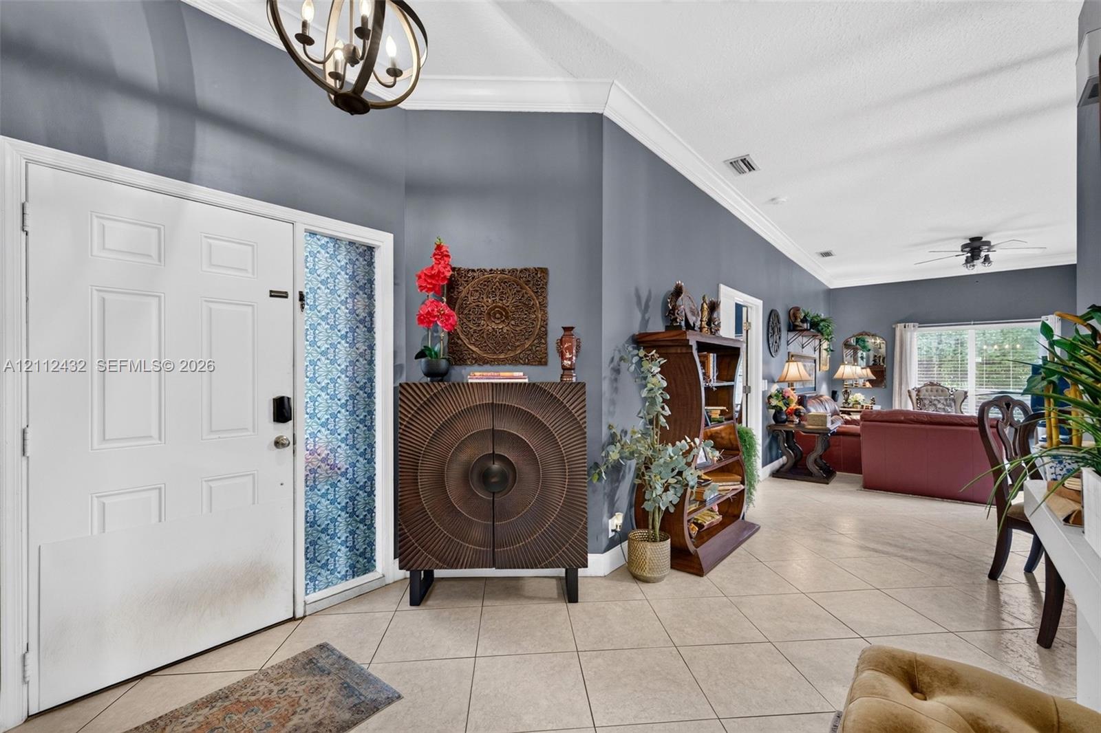 Foyer featuring a white front door with sidelight, vaulted ceilings with crown molding, light-toned ceramic tile flooring, and a decorative orb chandelier