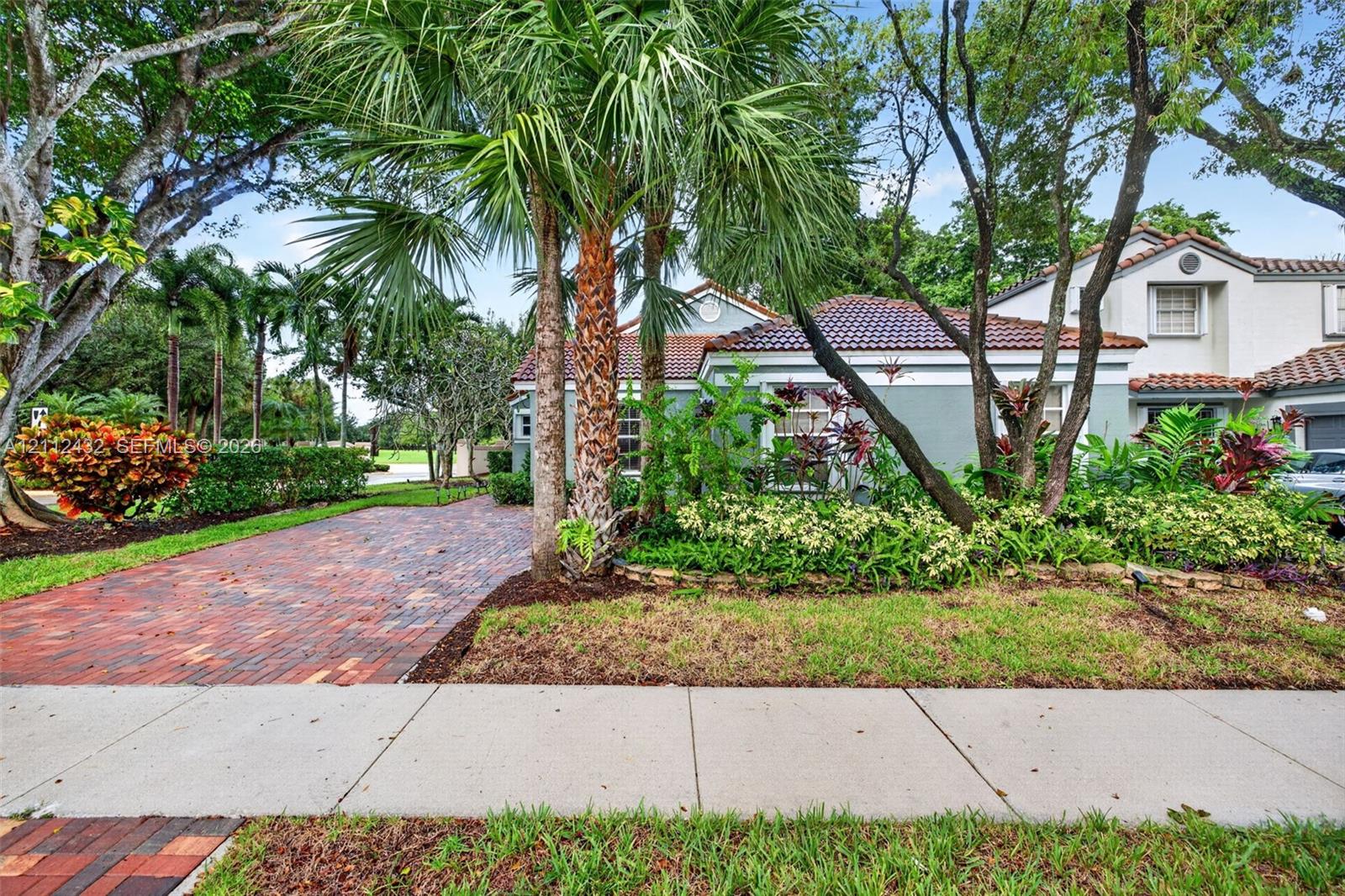 Exterior featuring a multi-toned brick paver driveway, clay tile roof, and mature tropical landscaping