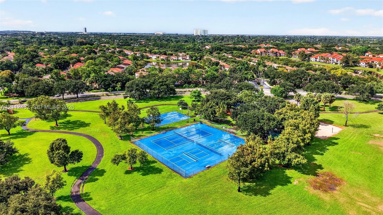 Extensive grounds featuring fenced tennis courts, winding paved paths, manicured lawns, and mature trees