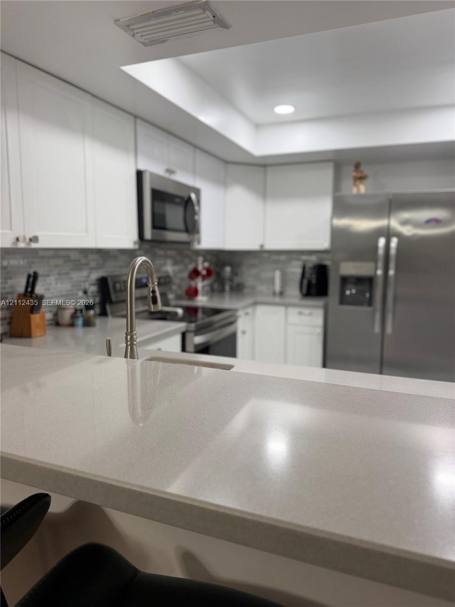 Kitchen featuring white cabinetry, solid-surface countertops, stainless steel appliances, and a tiled backsplash Kitchen featuring white cabinetry, solid-surface countertops, stainless steel appliances, and a tiled backsplash