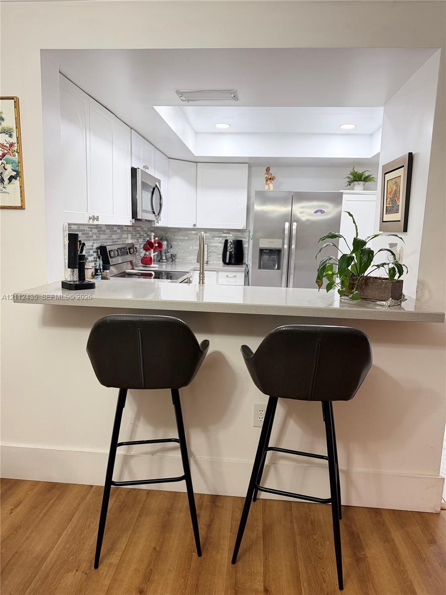 Kitchen featuring white cabinetry, solid-surface countertop with bar seating, tiled backsplash, recessed lighting, and stainless steel appliances Kitchen featuring white cabinetry, solid-surface countertop with bar seating, tiled backsplash, recessed lighting, and stainless steel appliances