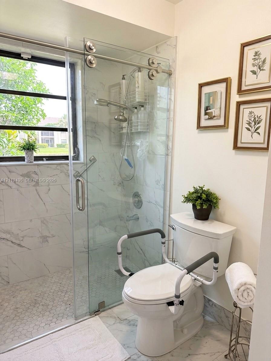 Walk-in shower featuring a sliding glass door, white stone-finish tile surround, hexagon floor tile, and chrome fixtures