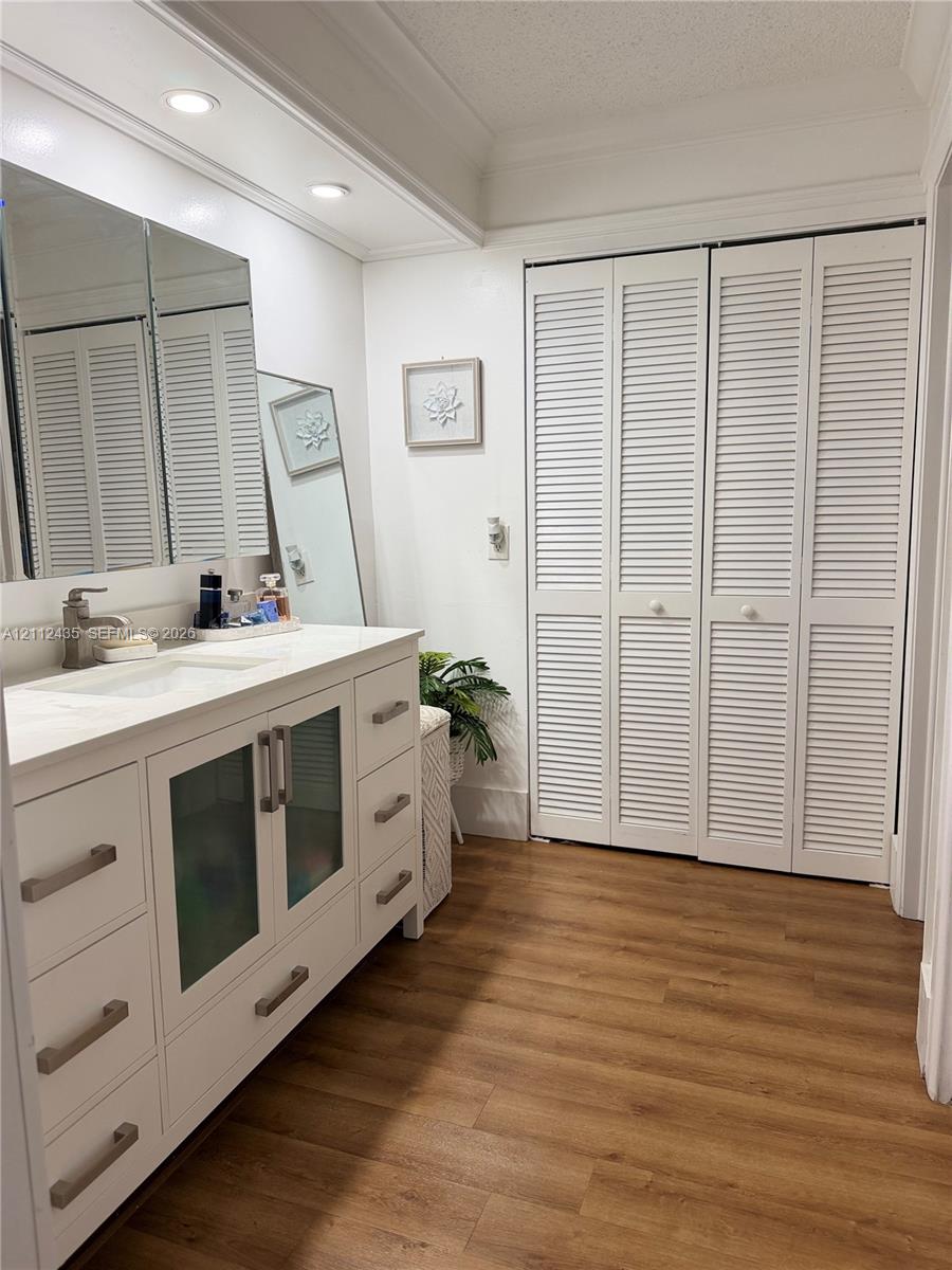 White vanity with integrated rectangular sink and stone-finish countertop, dual-mirrored medicine cabinet, recessed lighting, louvered bi-fold closet doors, and wood-finish flooring
