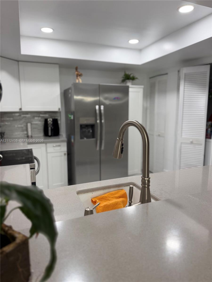 Kitchen featuring quartz countertops, undermount sink with arched pull-down faucet, white cabinetry, stainless steel side-by-side refrigerator, and recessed lighting Kitchen featuring quartz countertops, undermount sink with arched pull-down faucet, white cabinetry, stainless steel side-by-side refrigerator, and recessed lighting