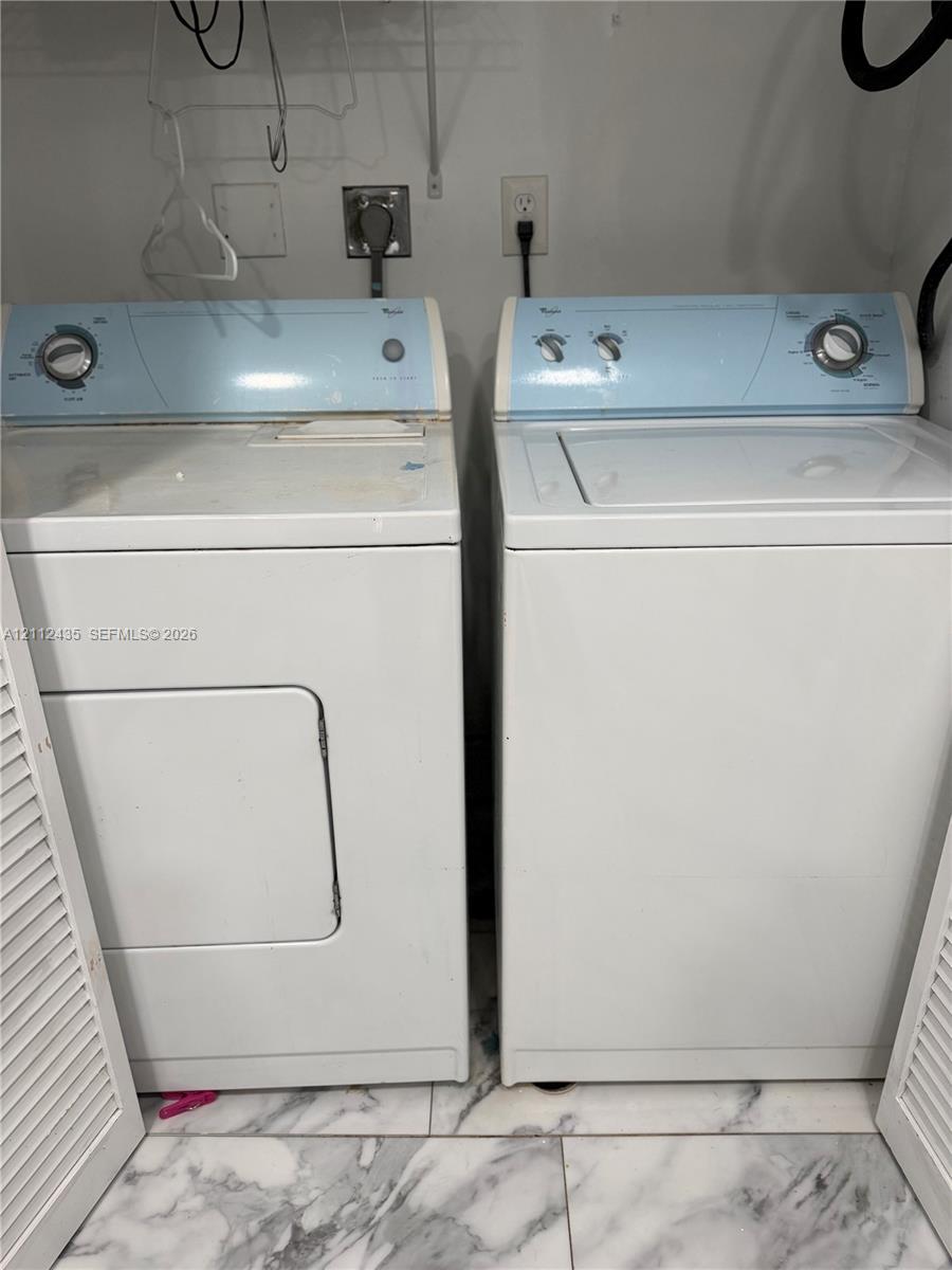 Laundry area featuring a top-loading washer, side-by-side electric dryer, louvered doors, and stone-finish tile flooring