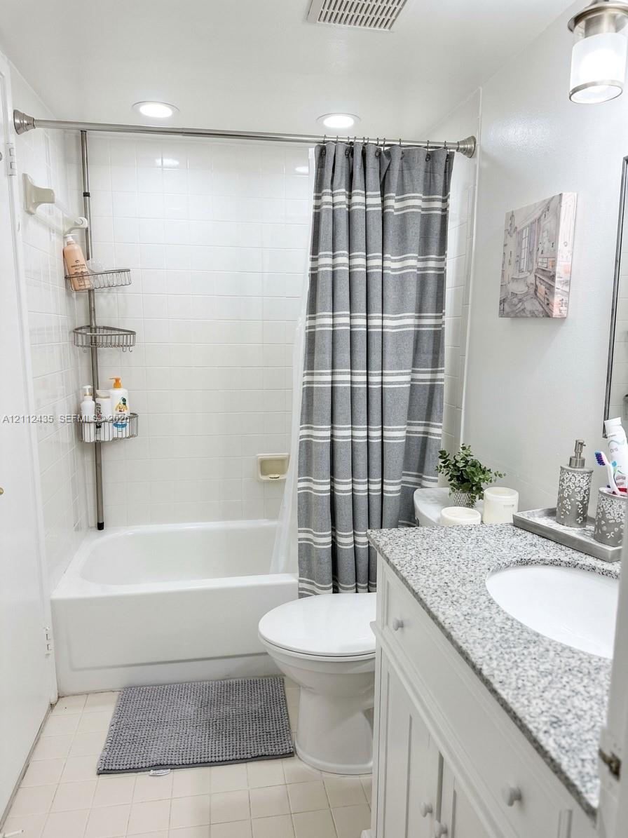 Bathroom featuring a vanity with a light-toned speckled countertop, an integrated sink, white cabinetry, a porcelain tub-and-shower combination with tiled surround, and recessed ceiling lighting
