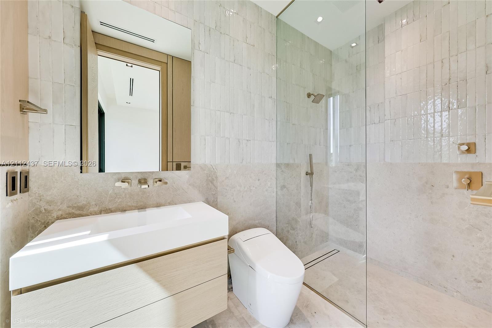 Floating vanity with integrated sink, glass-enclosed walk-in shower, wall-mounted brushed metal plumbing fixtures, and textured stone wall tile