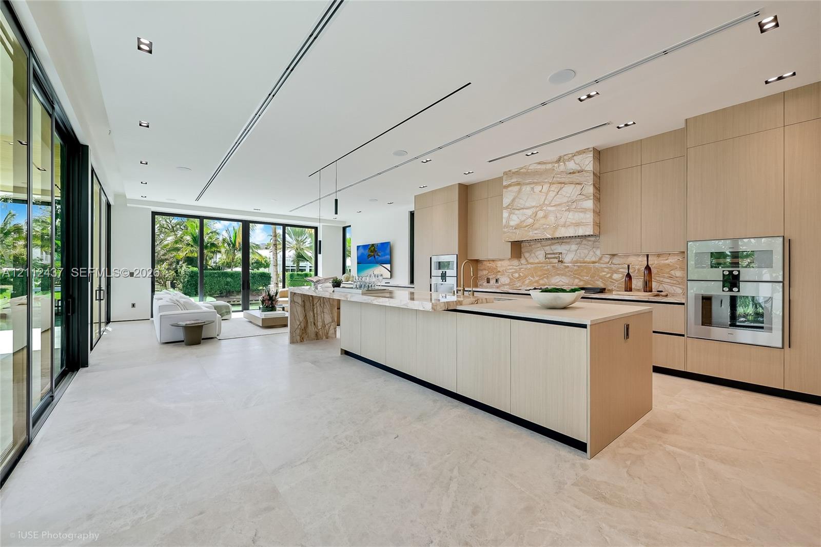 Floor-to-ceiling retractable glass walls, light wood-paneled ceiling with integrated recessed lighting, expansive stone flooring, and custom built-in shelving Floor-to-ceiling retractable glass walls, light wood-paneled ceiling with integrated recessed lighting, expansive stone flooring, and custom built-in shelving