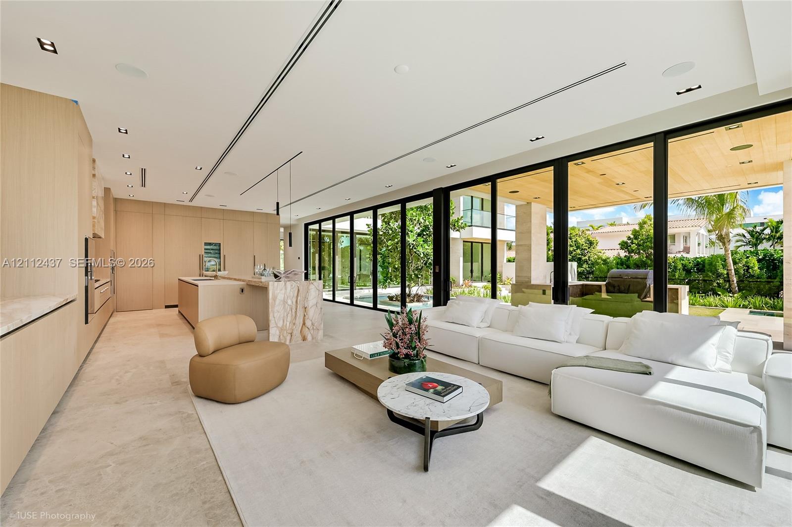 Floor-to-ceiling multi-panel glass doors, stone tile flooring, recessed ceiling lighting, and covered outdoor terrace with wood-plank ceiling