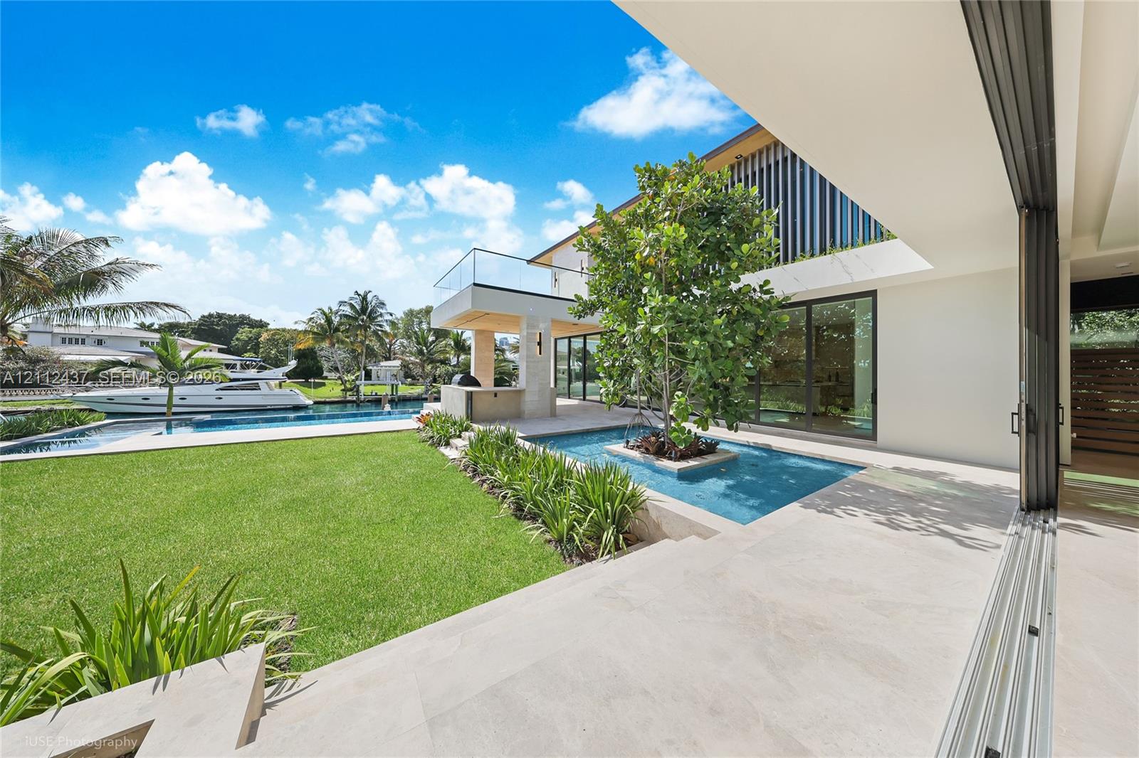 Outdoor terrace featuring a reflective water feature with a central tree, built-in stone kitchen, glass-railed balcony, and retractable wall panels
