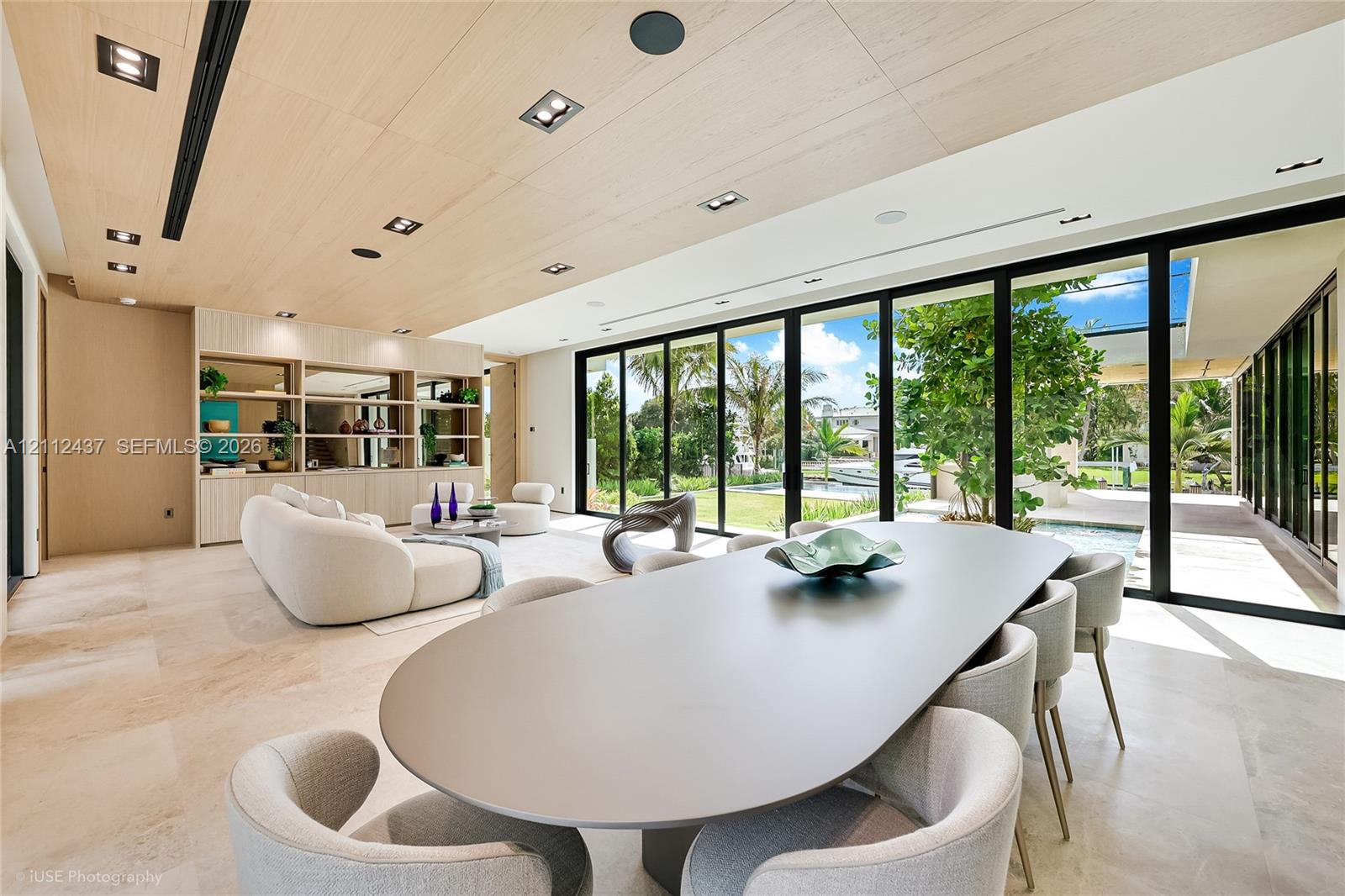 Open-concept interior featuring light wood-panel ceilings, large-format stone flooring, floor-to-ceiling glass sliding doors, and integrated recessed lighting Open-concept interior featuring light wood-panel ceilings, large-format stone flooring, floor-to-ceiling glass sliding doors, and integrated recessed lighting