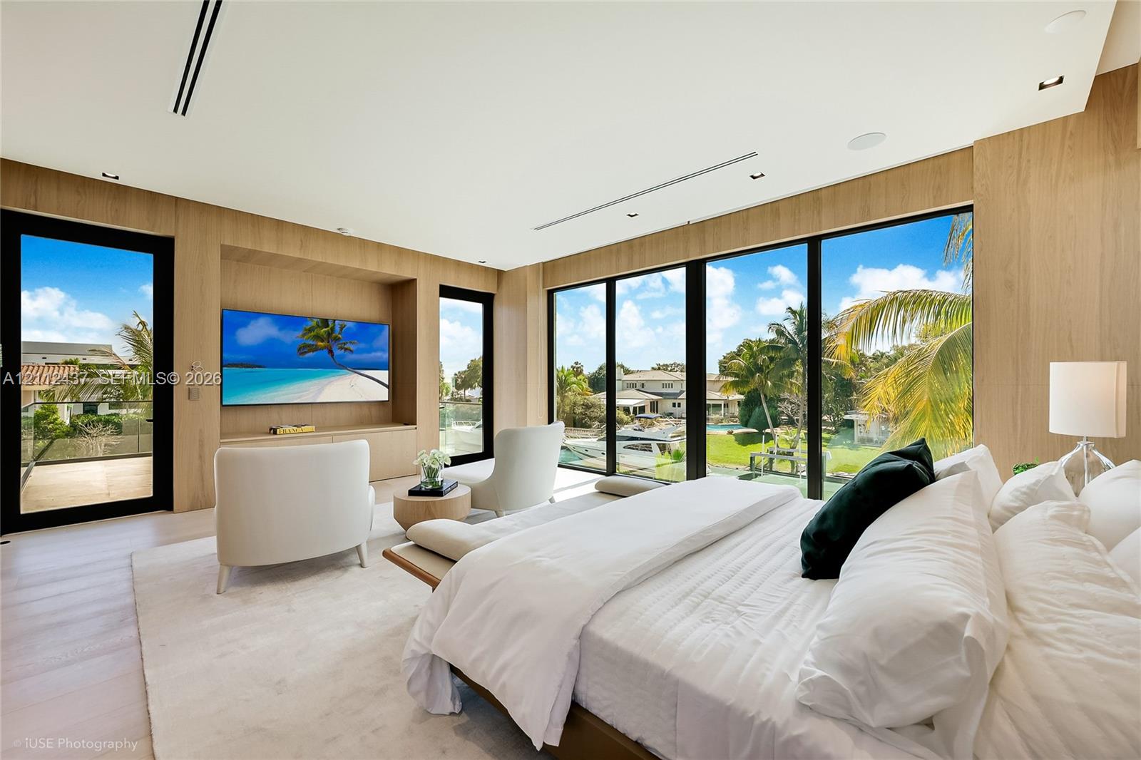 Floor-to-ceiling windows, wood-finish wall paneling, recessed lighting, built-in media console, and glass door access to a balcony