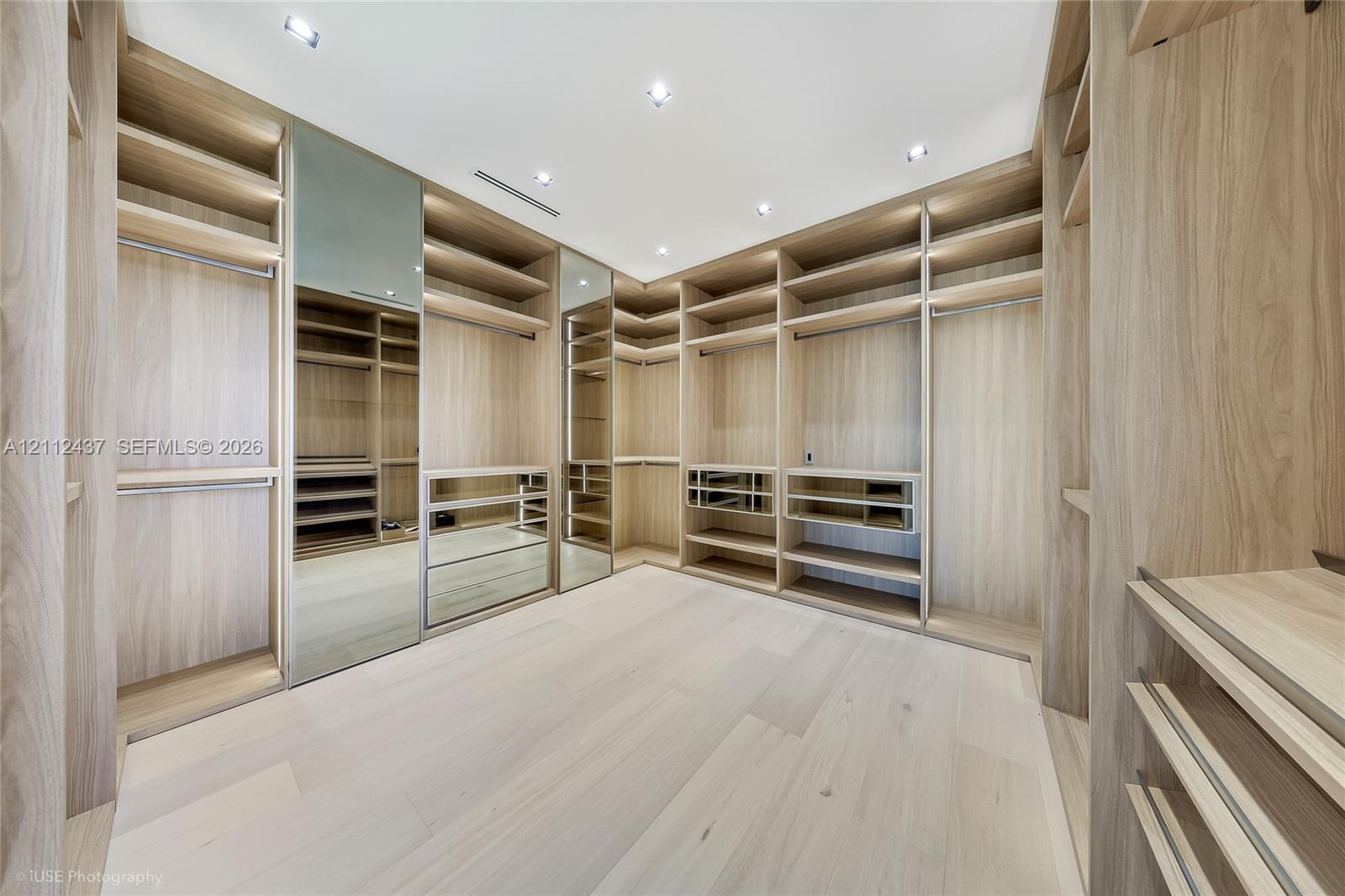 Custom built-in wood-finish cabinetry featuring extensive shelving, hanging rods, integrated mirrors, and recessed ceiling lighting throughout