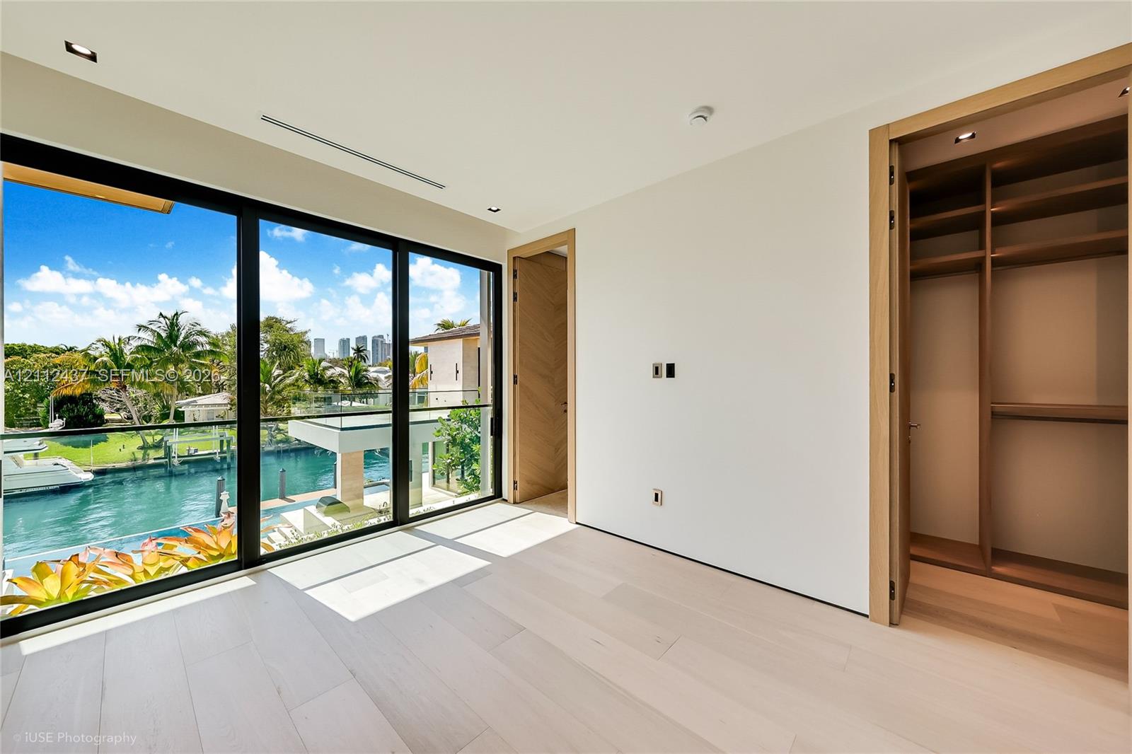 Floor-to-ceiling glass paneling, light wood-finish flooring, recessed lighting, and custom built-in wood closet shelving