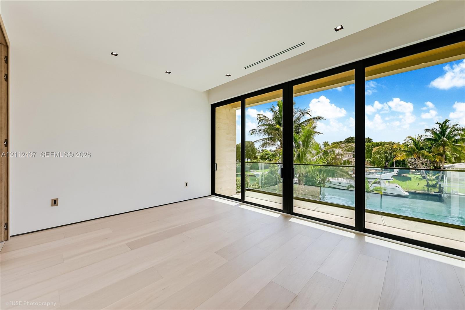 Light-filled room featuring wood-finish flooring, recessed lighting, and floor-to-ceiling multi-panel sliding glass doors with access to a balcony with glass railings