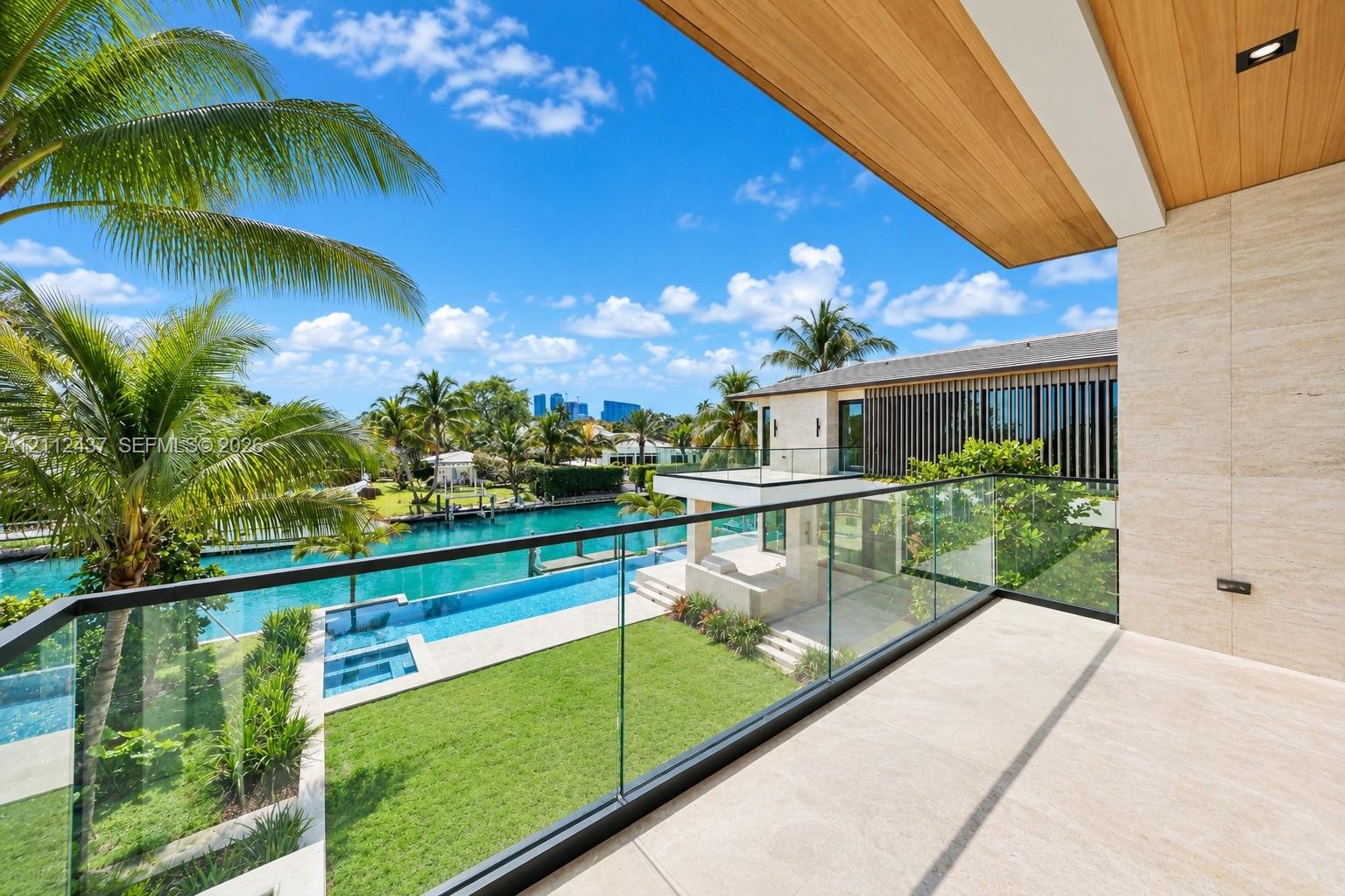 Covered balcony featuring stone flooring, wood-plank ceiling, and a frameless glass railing overlooking the waterfront property, swimming pool, and landscaped lawn Covered balcony featuring stone flooring, wood-plank ceiling, and a frameless glass railing overlooking the waterfront property, swimming pool, and landscaped lawn