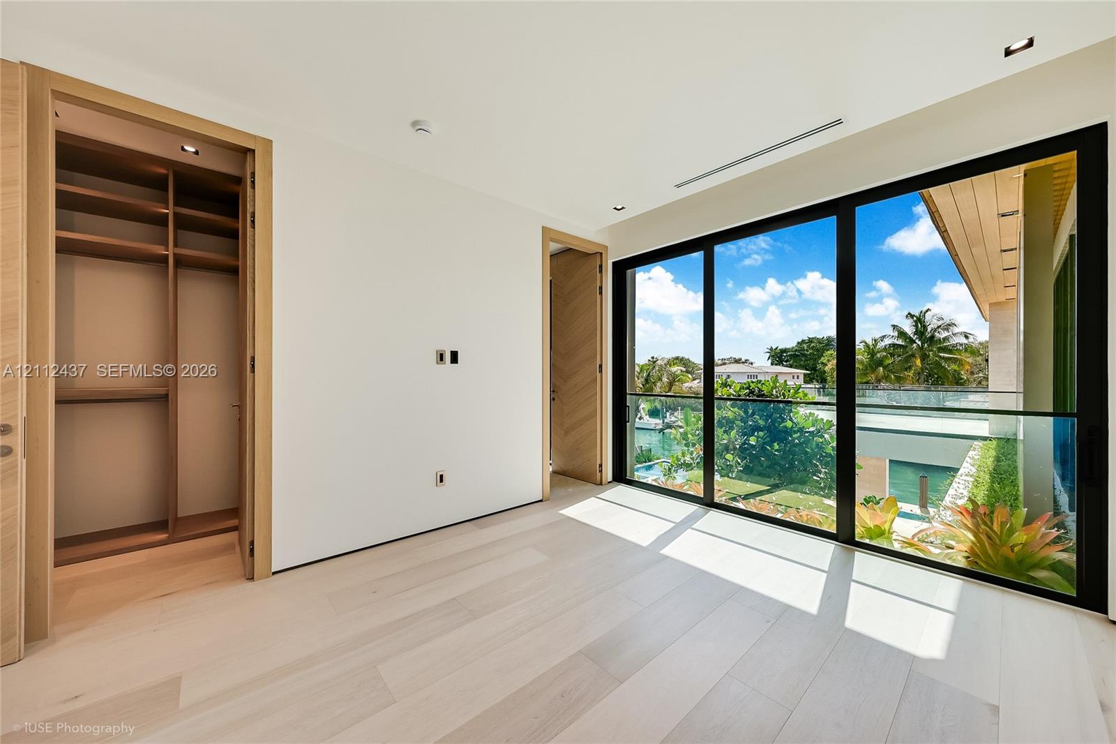 Light-toned wood-finish flooring, built-in wooden closet cabinetry, floor-to-ceiling glass sliding doors, and recessed ceiling lighting