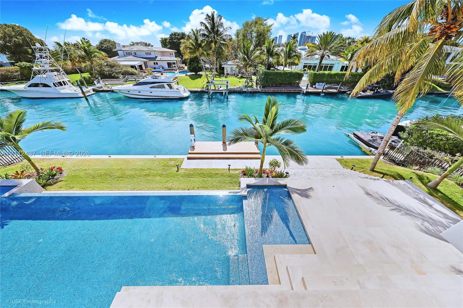 Waterfront estate featuring a paved terrace, swimming pool with integrated sun shelf, private boat dock, and manicured landscaping