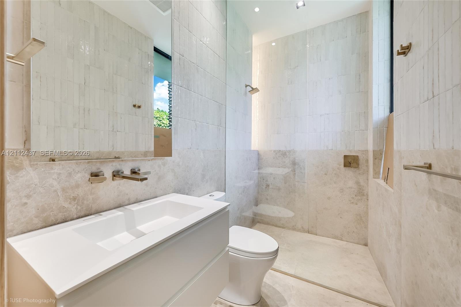 Floating vanity with integrated sink and wall-mounted faucet, walk-in shower with glass partition, floor-to-ceiling tiled walls, and recessed lighting