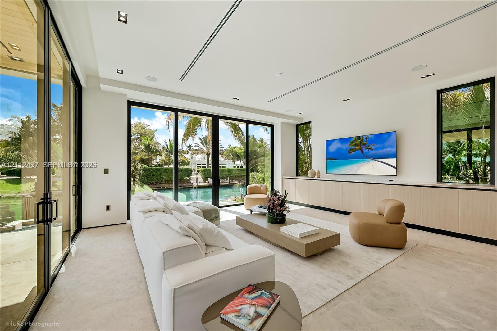 Custom light-finish cabinetry, natural stone backsplash and range hood surround, integrated stainless steel appliances, stone slab countertop, and recessed ceiling lighting