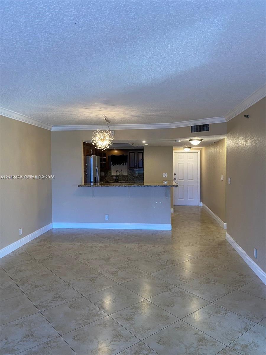 Open-concept area featuring stone-finish floor tiling, crown molding, a decorative multi-bulb chandelier, and a kitchen pass-through breakfast bar Open-concept area featuring stone-finish floor tiling, crown molding, a decorative multi-bulb chandelier, and a kitchen pass-through breakfast bar