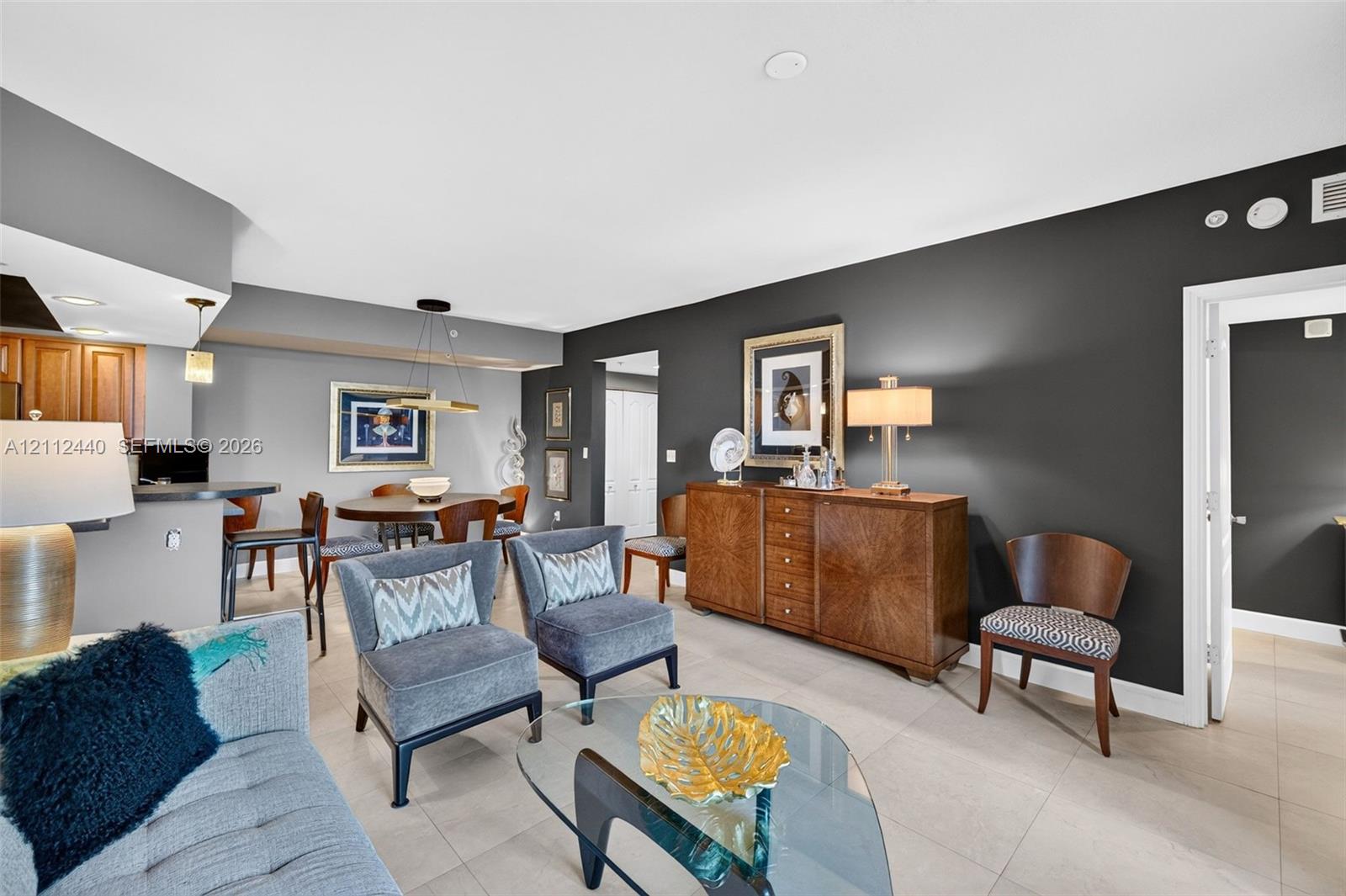 Open-concept living space featuring high-contrast charcoal accent walls, large-format porcelain flooring, a tiered breakfast bar (chandelier does not convey)