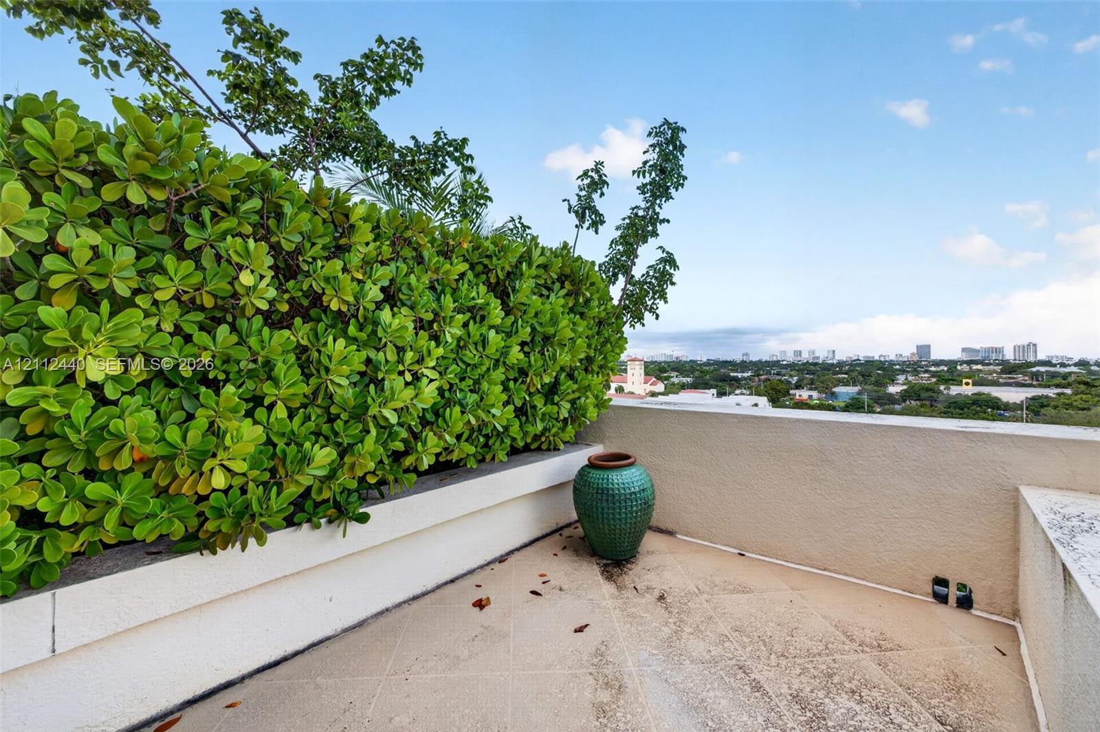 Rooftop terrace featuring concrete tiled flooring, stucco perimeter walls, and a built-in planter with mature hedge greenery